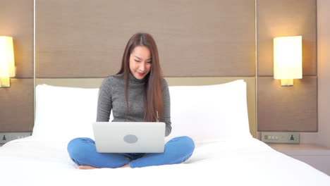 A-pretty-young-woman-enjoys-sitting-on-the-bed-while-working-on-her-laptop