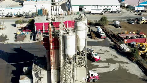 aerial pan right shot of silos on a industrial complex with semi trucks, humans working and heavy equipment moving