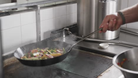 chef caucásico fritando verduras en una sartén en la cocina, en cámara lenta