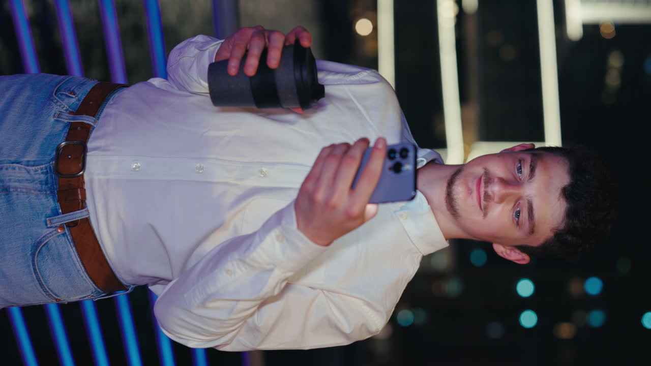 Man holding phone and cup at night