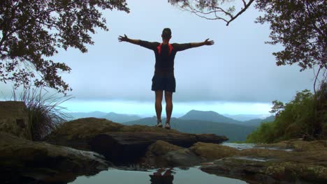 Joven-Parado-En-La-Cima-De-La-Cascada,-Disfrutando-De-La-Vista-A-La-Montaña-En-El-Circuito-Warrie,-Parque-Nacional-Springbrook,-Australia