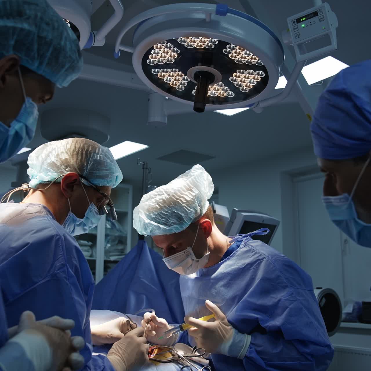 Two surgeons using metal tools collaborating at operation. Doctors' assistants standing at foreground watching the procedure