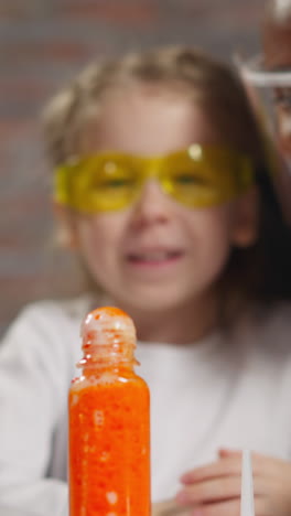 little girl student discusses swirling orange liquid reaction in small bottle with asian and bearded african-american scientists at lesson closeup
