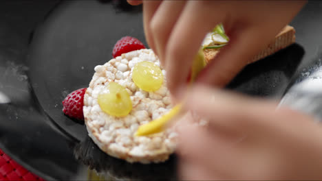 Kind-Legt-Obst-Auf-Reiskuchen,-Um-Ein-Smiley-Gesicht-Zu-Machen