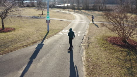 An-aerial-tracking-of-a-man-on-an-electric-skateboard-in-an-empty-park-on-a-sunny-day