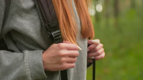 close-up of woman hiking through lush forest, gripping backpack straps with long nails and long hair flowing over shoulders, wearing gray sweatshirt and focused expression