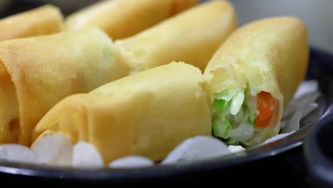 a detailed view of golden spring rolls filled with fresh vegetables, neatly arranged on a black plate.