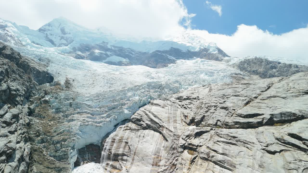 A spectacular aerial drone shot rises up the face of a massive, melting glacier, revealing the vast ice fields and snow-capped peaks that feed Laguna 513 in the Peruvian Andes
