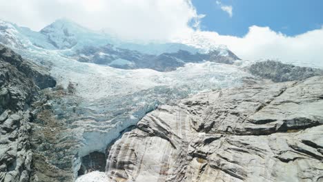 a spectacular aerial drone shot rises up the face of a massive, melting glacier, revealing the vast ice fields and snow-capped peaks that feed laguna 513 in the peruvian andes