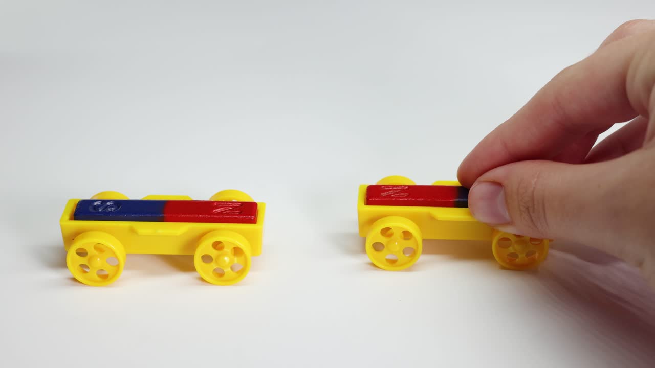 Two magnetic toy cars interact on a white surface, illustrating magnetic forces with colorful blocks and hands adjusting positions