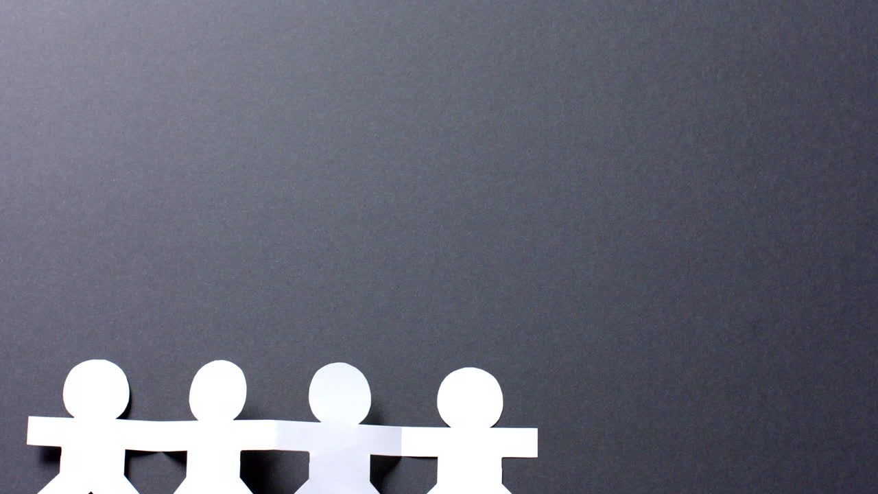 Close up of people holding hands made of white paper on gray background with copy space