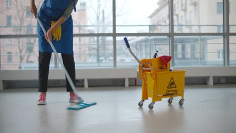 uniformed cleaner wiping floor using mop and cart in business center