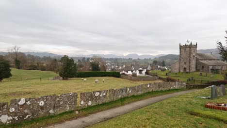 St-Michael-and-All-Angels-Church-in-Hawkshead,-showing-fields-and-grazing-sheep-Cumbria,-UK