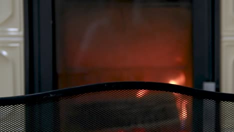 Fireplace-screen,-mesh-in-front-of-traditional-tiled-stove-with-burning-wooden-logs,-interior-winter-scene