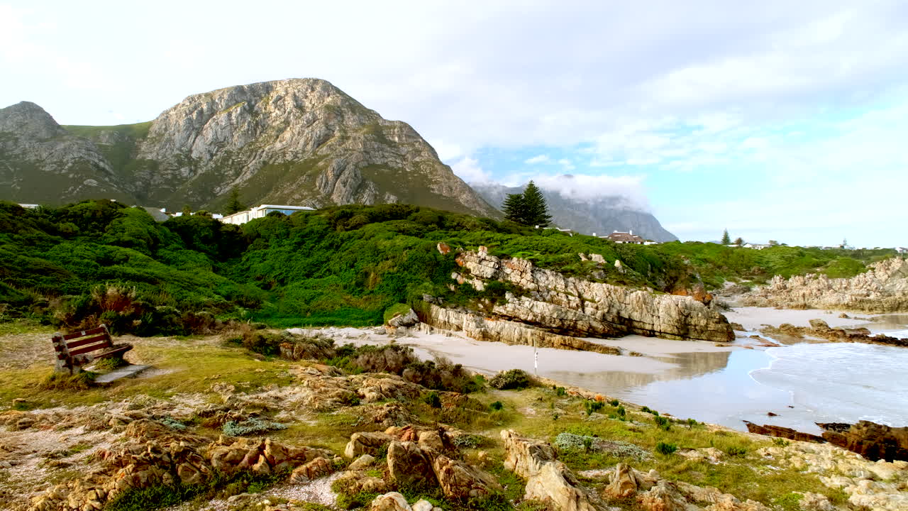 Bench on Hermanus coastline overlooking beach and ocean near sandy coves, Klein River mountain background, Cape Whale Coast