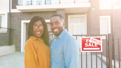 portrait of happy african american married couple standing at new house at suburb and smiling cheerfully