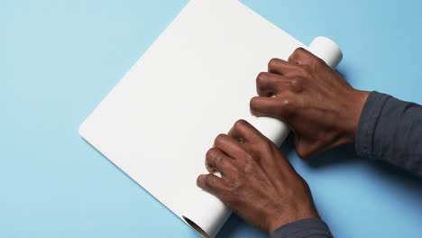 video of hands of african american man with rolling up white paper on blue background