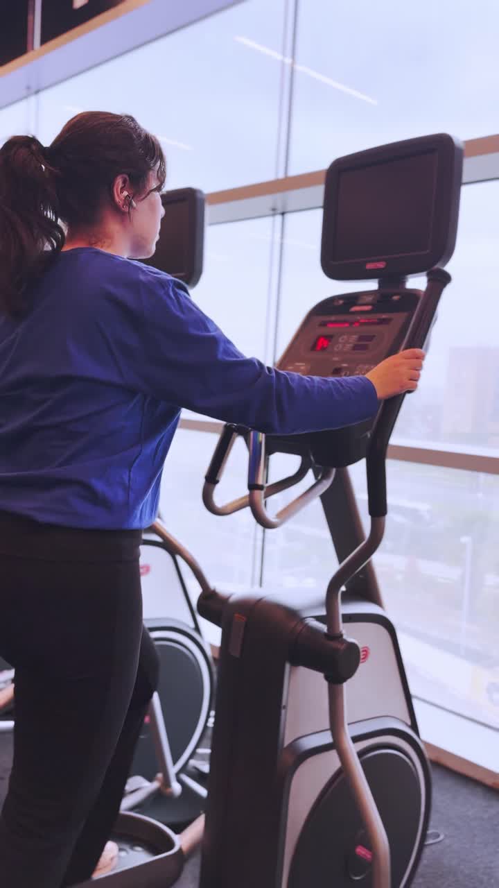 Young woman working out on elliptical trainer in gym