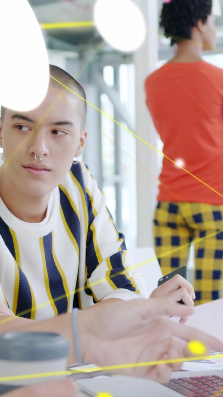 Vertical video: Man tapping phone, using laptop, peer watching notes, yellow lines linking business