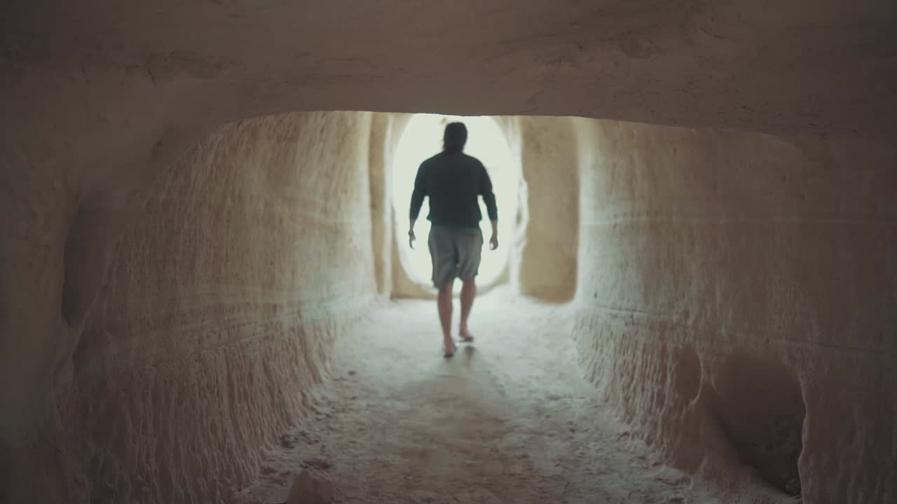 멋지고 젊은 남자가 외국에서 휴가를 보내는 동안 사람이 만든 동굴에서 나오는 느린 동영상