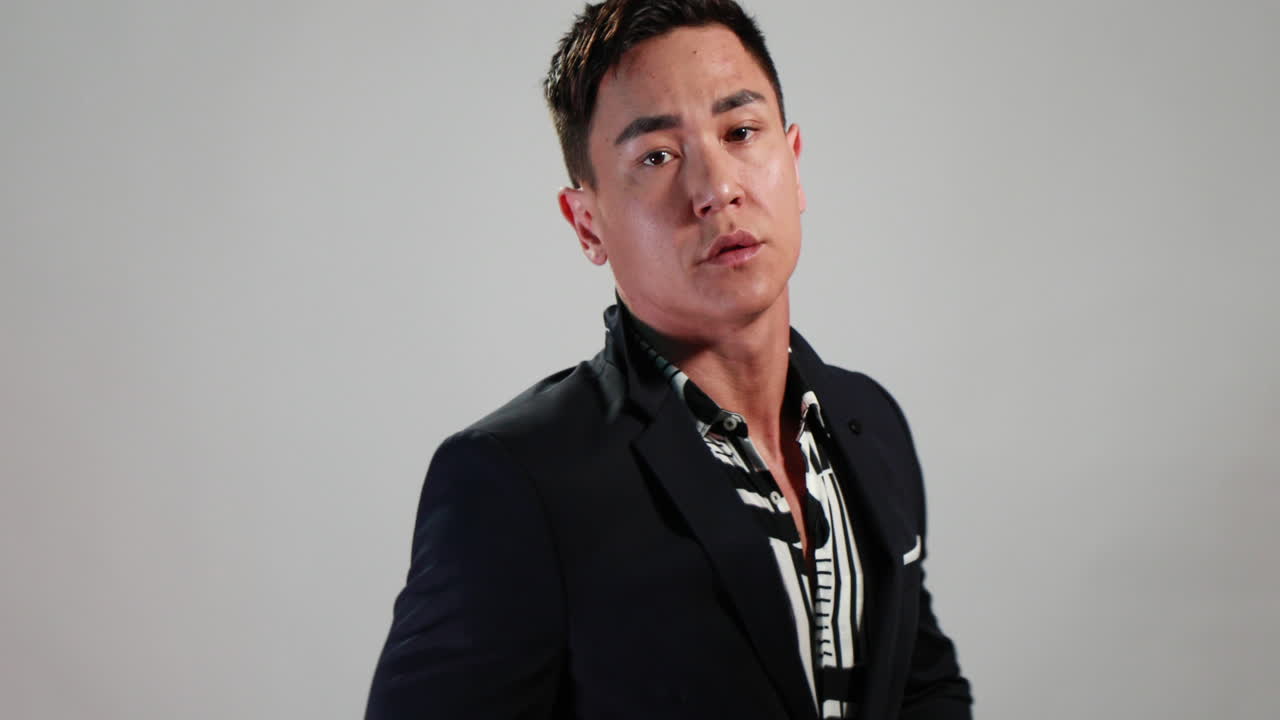 슬로모션의 매력적인 아시아 모델은 재킷이 있는 흰색 배경 앞에 있는 웹 사이트 또는 소셜 미디어를 위한 전자 상거래 사진 촬영 중에 포즈를 바꾸고 포즈를 변경합니다.