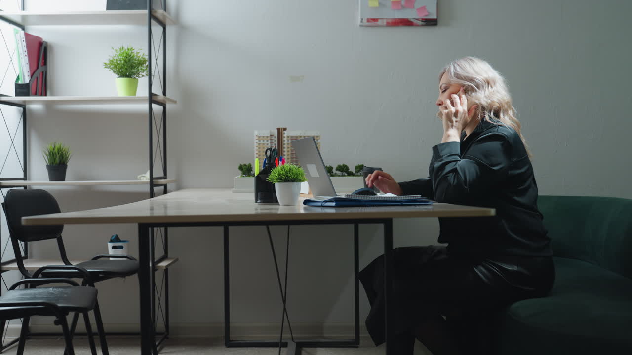 Side view of business expert seated in office answering phone call while multitasking with laptop and client communication, surrounded by model building