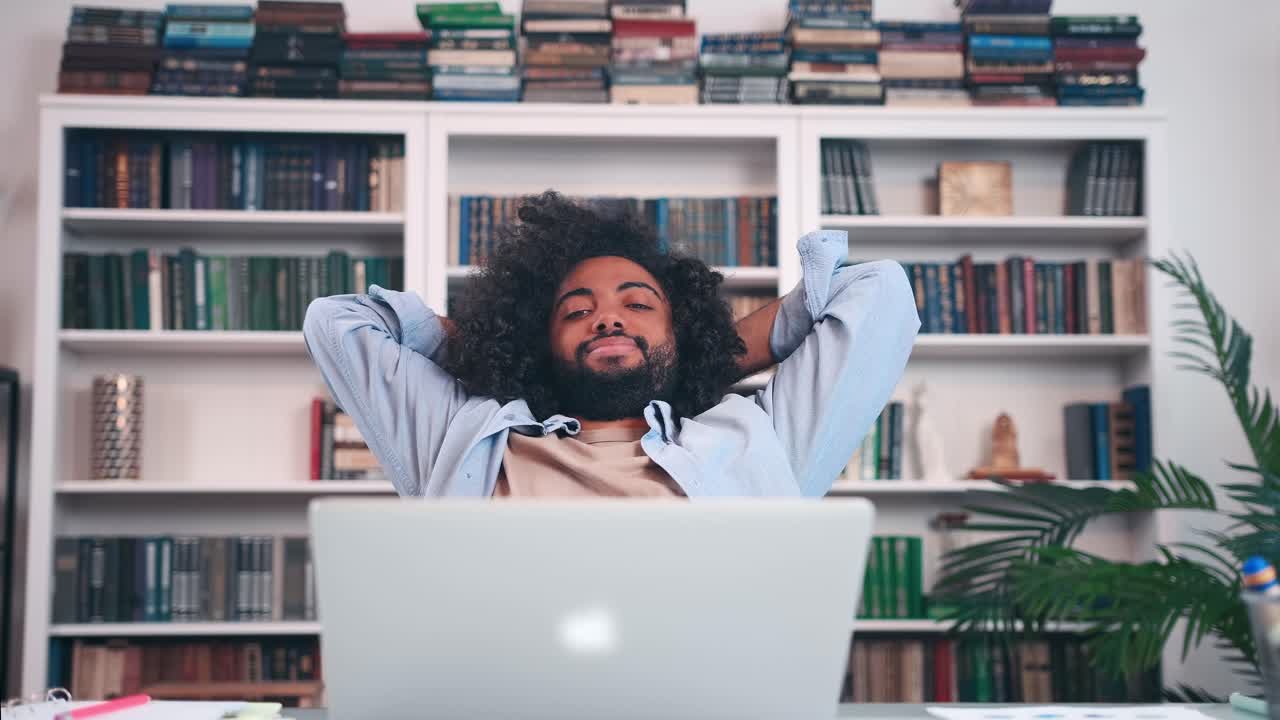 Homem árabe freelancer alegre recosta-se na cadeira após o trabalho de escritório.