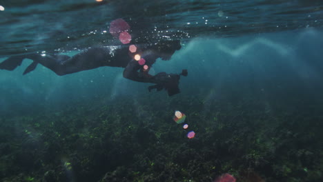 photographer floats at the surface of the ocean balancing camera facing down as the glide through sparkling dazzling open water