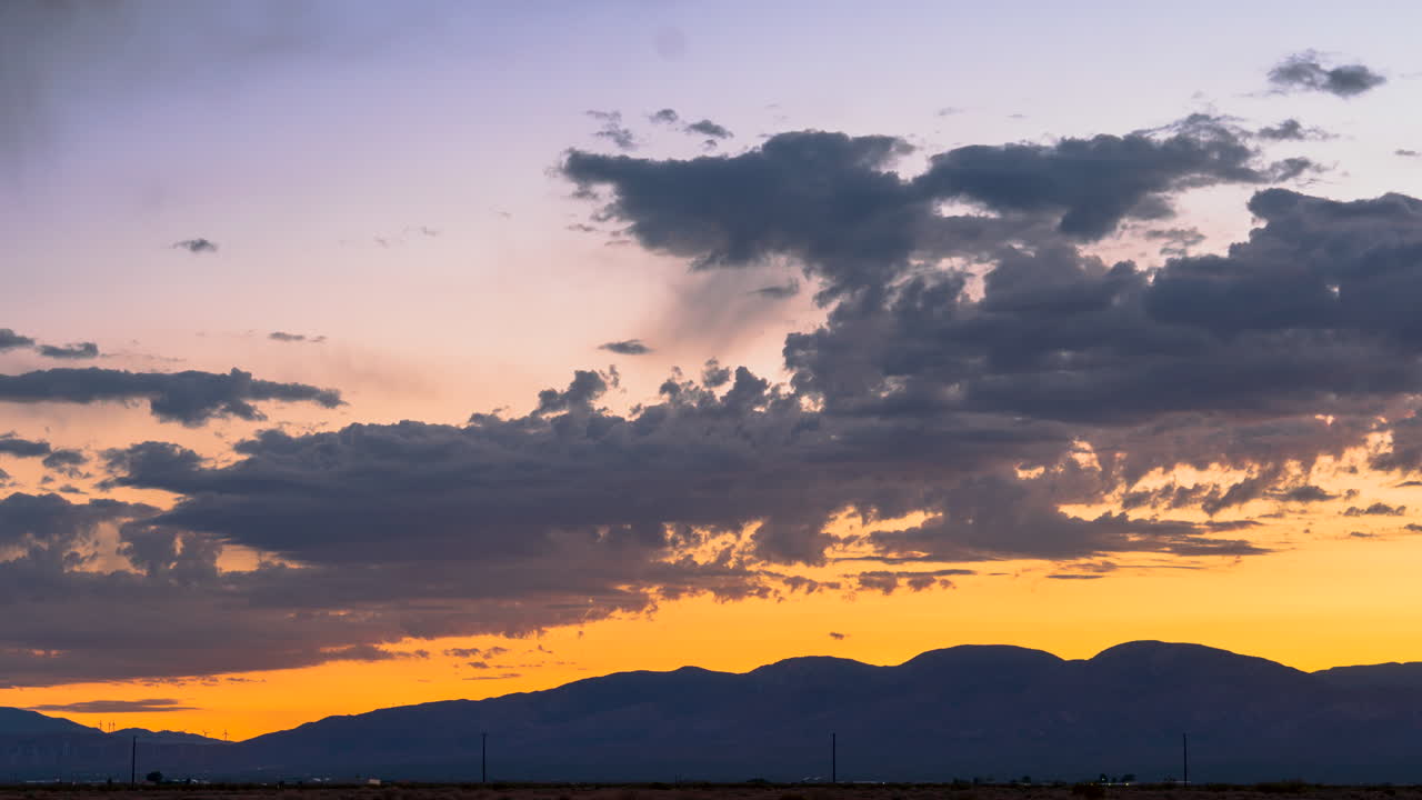 colorido carmesí y dorado cloudscape mientras el sol se pone más allá de la silueta de montañas escarpadas - lapso de tiempo estático