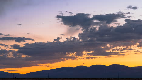 colorful crimson and golden cloudscape as the sun sets beyond the silhouette of rugged mountains - static time lapse