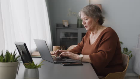 Mujer-Enfocada-Escribiendo-En-La-Computadora-Portátil-Sentada-En-El-Escritorio-En-Casa-1