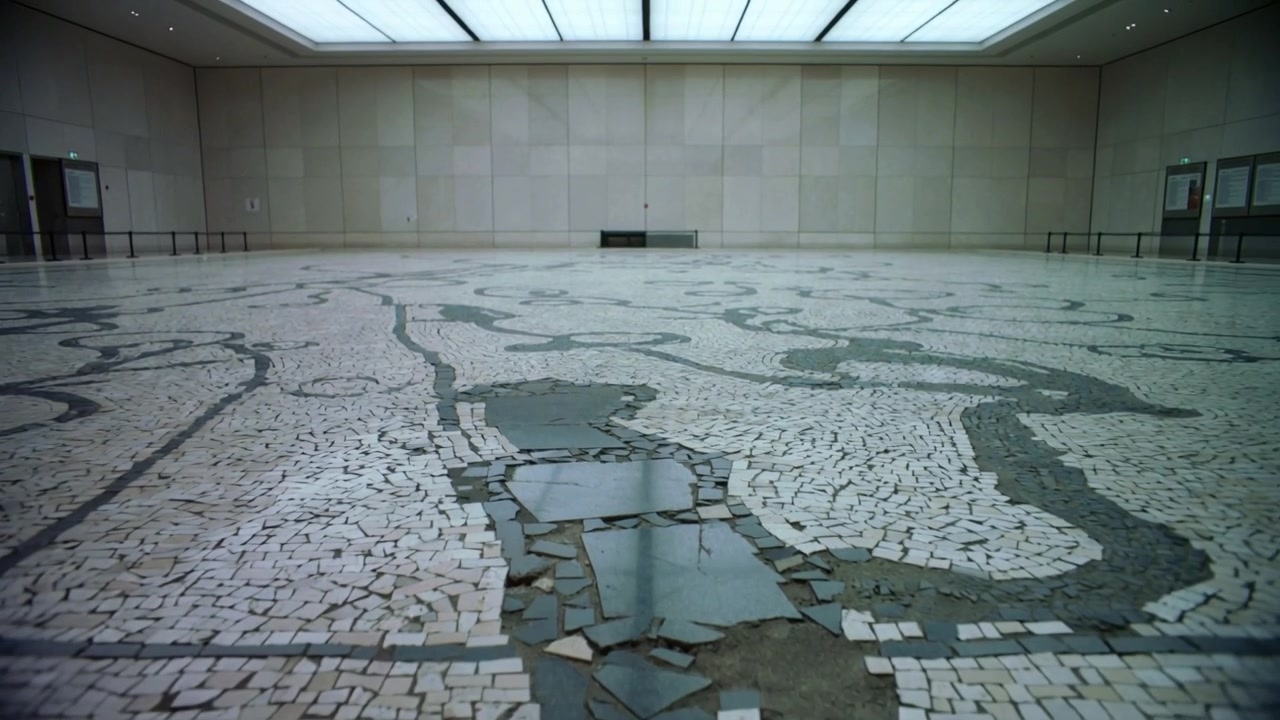 Telecamera che si allontana rivelando un pavimento a mosaico decorato in una galleria museale, documentando le piastrelle danneggiate.