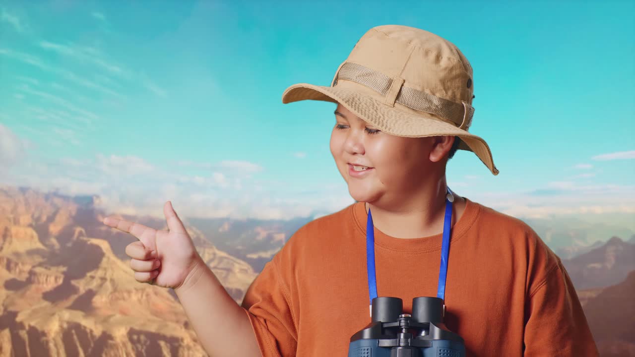 Asian Boy With A Hat And Binoculars Smiling And Pointing To Side While Traveling At The Top Of Mountain. Boy Researcher Examines Something, Travel Tourism Adventure Concept, Close Up