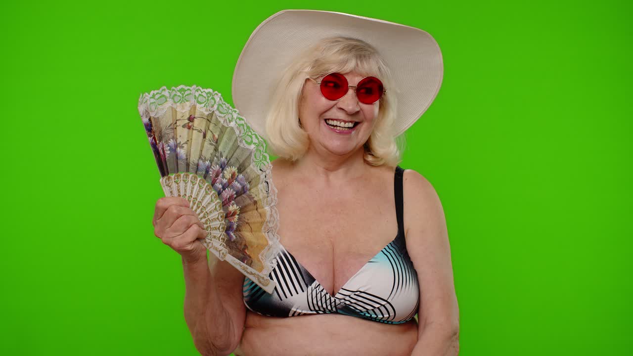 수영복 브래지어를 입은 노인 여성 관광객이 열이나 막힌 상태에서 숨을 내쉬고, 손을 스스로 팬으로 흔들고 있습니다.