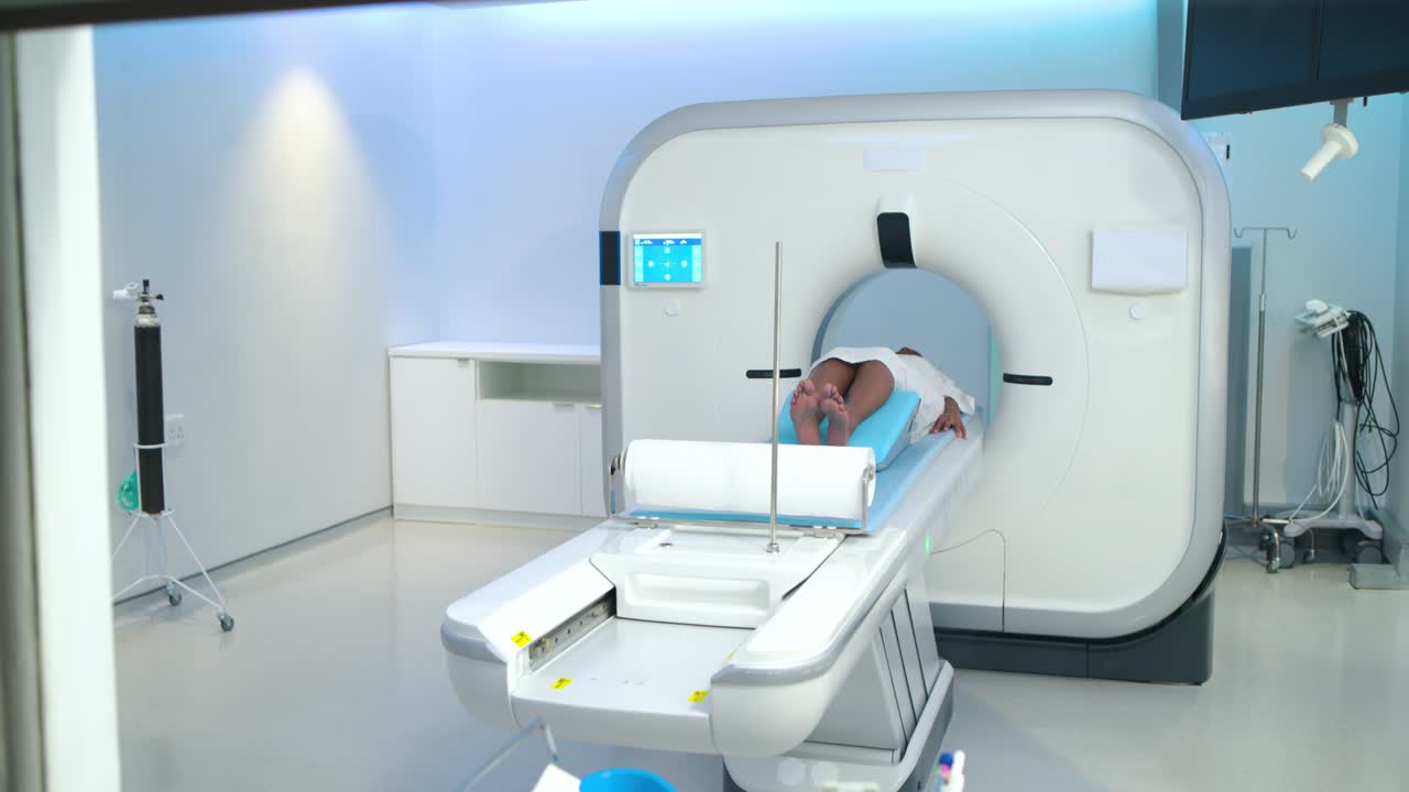 Tech's hand pointing at brain scans, causing pan and sliding table to position patient in gantry