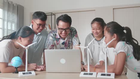 middle school classroom: enthusiastic asian teacher use laptop computer explains to a brilliant young children how wind turbines work. kids learning about eco-friendly forms of renewable energy