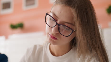 joven con gafas mira hacia abajo en la biblioteca. concentrada estudiante estudia lección en clase universitaria. auto-preparación para exámenes en la universidad