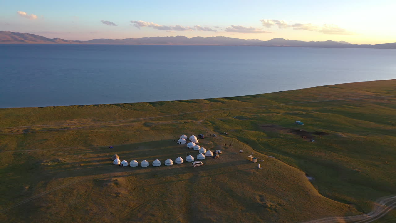 юрты выстроились вдоль берега в захватывающем дух виде с воздуха на закате над озером сон-куль, кыргызстан
