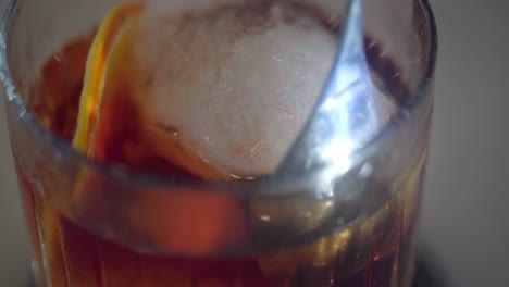 revolviendo un cóctel con hielo y una rodaja de naranja