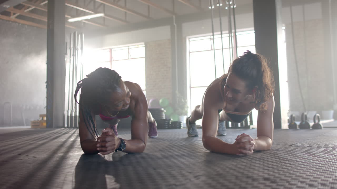 Women planking on gym floor, engaging in fitness training and smiling together