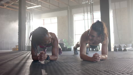 women planking on gym floor, engaging in fitness training and smiling together