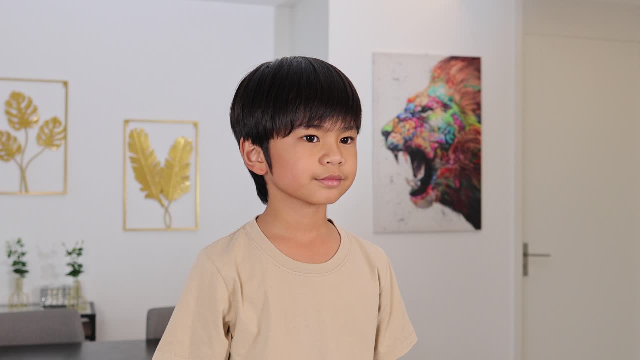 Young Asian boy blocks ears, shakes head, reacts to noise in bright modern home interior