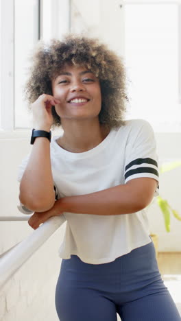 vertical video: smiling woman in yoga pilates studio leaning on barre, wearing fitness attire