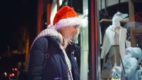 una mujer con un sombrero de santa mira una ventana de una tienda por la noche.