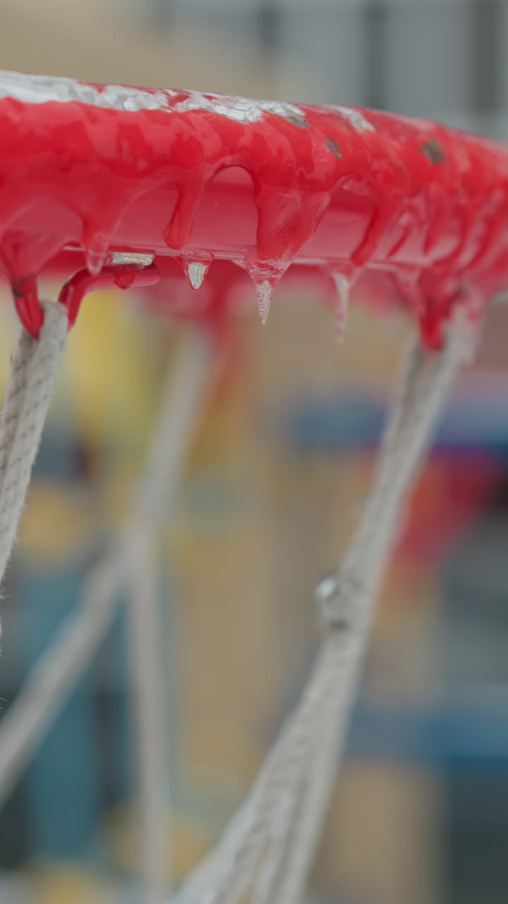 에서 매달린 아이스클과 배경에 흐릿한 눈 인 놀이터가 있는 얼음으로 된 농구 허프의 클로즈업, 시즌 동안 겨울과 추운 날씨의 본질을 포착합니다.