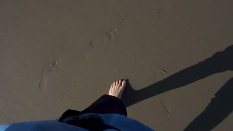 Persönlicher-Blick-Auf-Die-Füße-Eines-Mannes,-Der-Im-Schatten-Der-Abendsonne-Am-Sandstrand-Spaziert