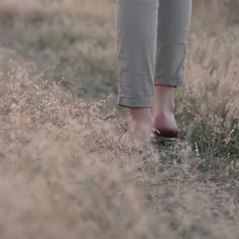 the legs of a woman in flip flops walk along the road between the thickets of grass