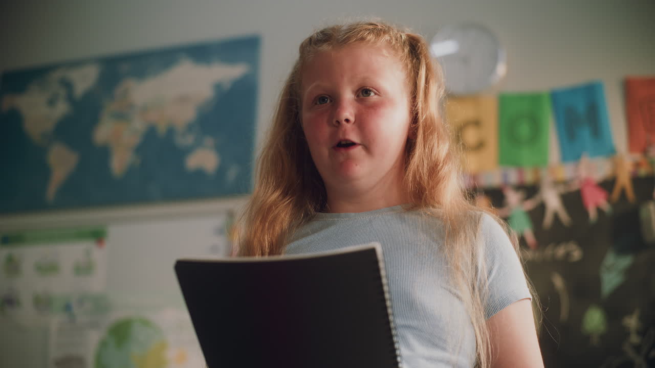 Muslim Primary School Girl Wearing Hijab Sitting at the Desk Writing School Test in Notebook