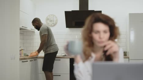 hombre negro limpiando la mesa en la cocina abierta. mujer bonita bebiendo café por la mañana