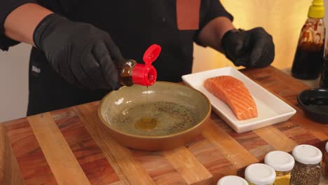 professional chef preparing marination sauce ingredients by pouring sesame oil and soy sauce into mixing bowl, with a fresh raw salmon fillet on the side